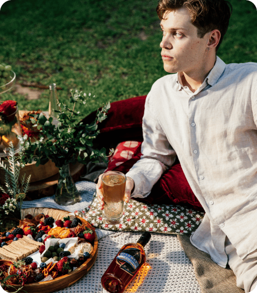 a man sitting on the grass with a picnic blanket with food and drinks
